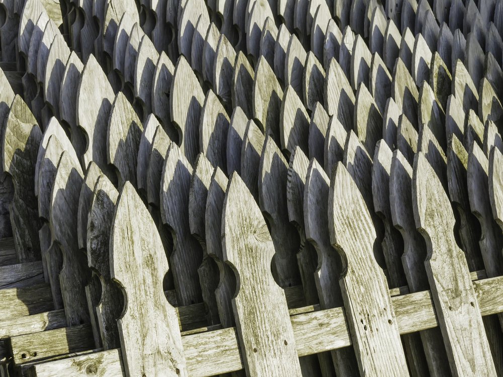 Pattern of weathered wooden fence posts, shaped like arrowheads, near sunset